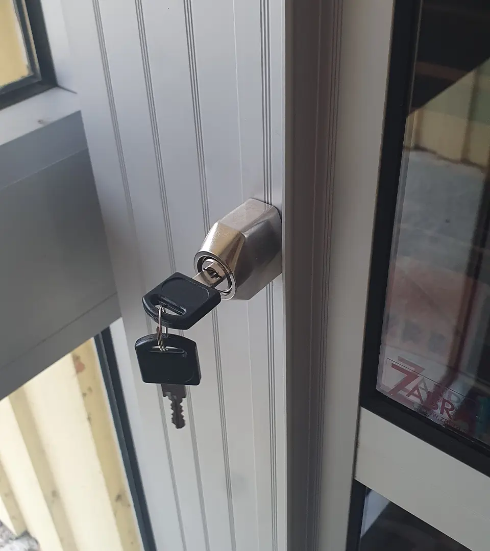 nyckel2 Två svarta nycklar sätts in i låset på en vit dörr eller ett vitt fönster med metallkarm.