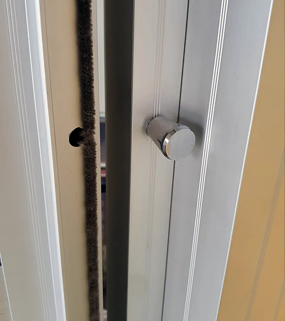 snäpp1 Närbild av en dörrkarm av metall med en rund bult utdragen och en luddig tätningslist längs kanten.