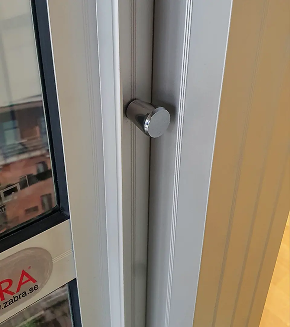 snäpp2 Närbild av en metallregel på kanten av en fönsterkarm, med en del av ett klistermärke med texten "ZABRA" synligt på glaset.