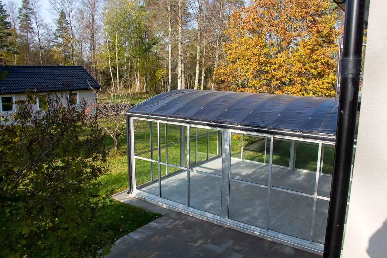 inglasat uterum med kupat tak i en trädgård med träd och växter runtomkring